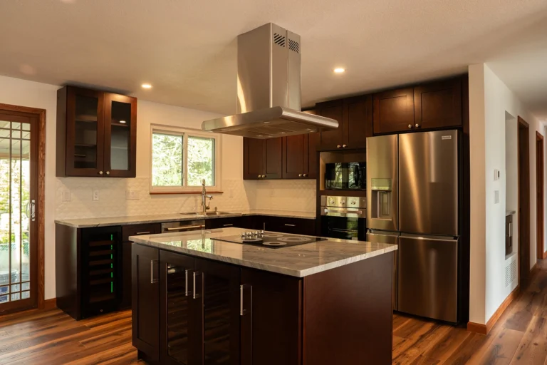 Remodeled kitchen showing dark perimeter cabinetry, built-in stainless steel appliances, and a white tile backsplash.