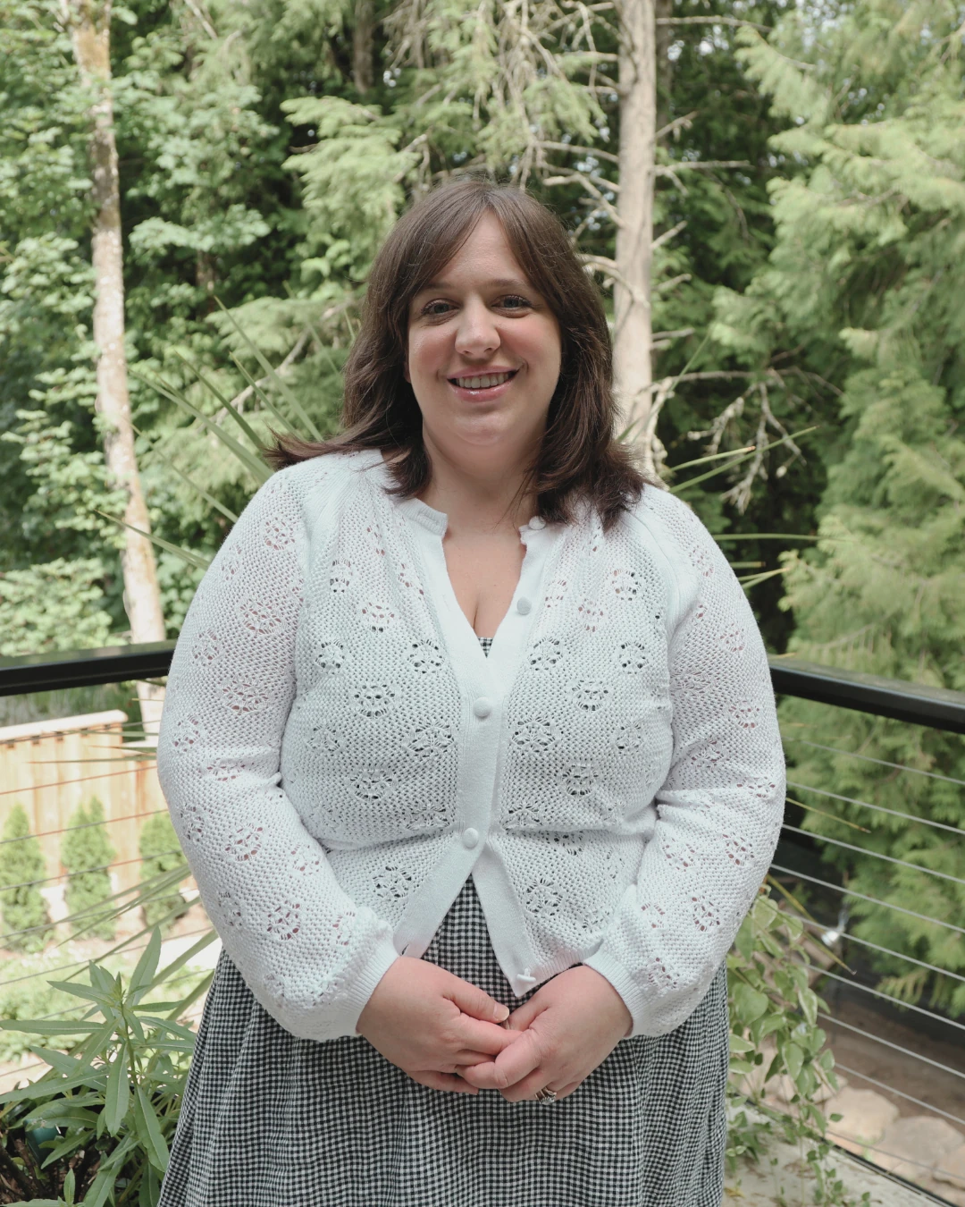 Ashley, office manager, standing outdoors on a balcony with trees in the background.