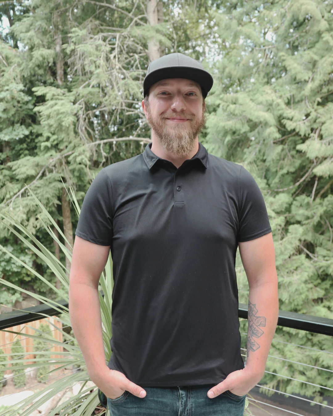 Matt, project manager, standing outdoors on a balcony with greenery in the background.