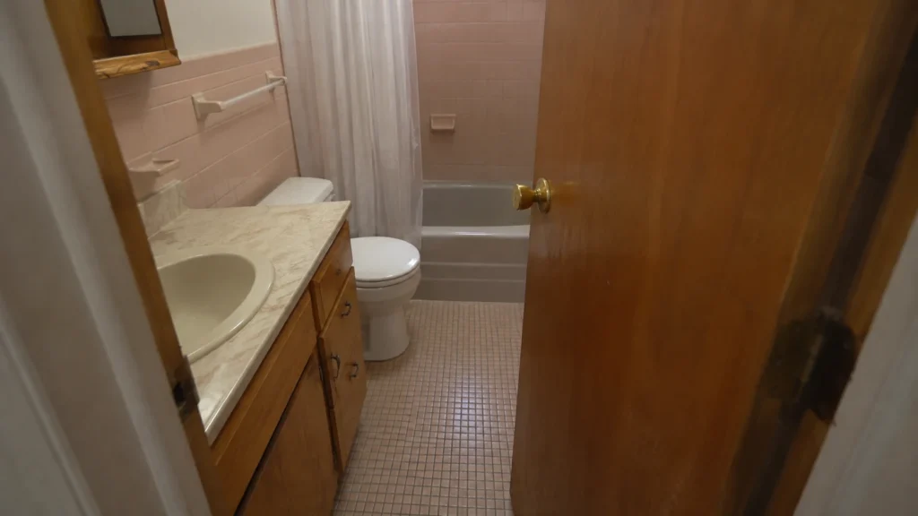 Cramped bathroom with an inward-swinging door crowding the vanity and toilet.